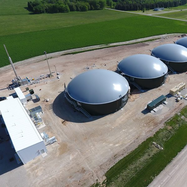 Aerial view of large biogas storage tanks in a rural area.