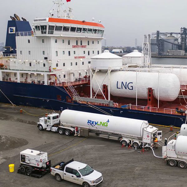 Ship docked with LNG tanker trucks nearby.